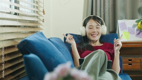 Young Asian Woman Listening to Music with Headphones Relaxing on Sofa at Home Smiling Happily