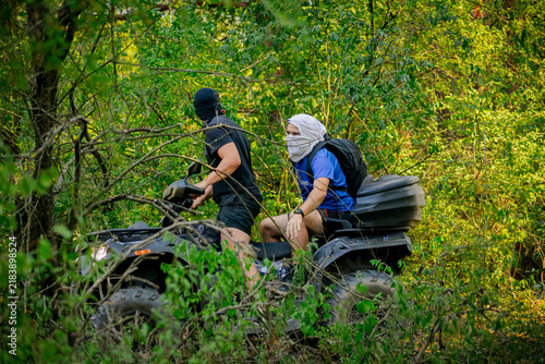 Riders on an ATV quad bike drive an off-road trail in a lush forest