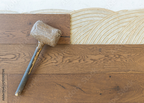 Rubber mallet on brown oak parquet planks during hardwood flooring installation, top view