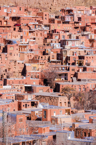 Traditional red mud-brick houses of Abyaneh village, Iran, built on a mountainside with rocky peaks in the background. Historic Persian village, unique earthen architecture and cultural heritage