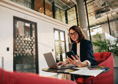 Smiling businesswoman using a smartphone and laptop at the office
