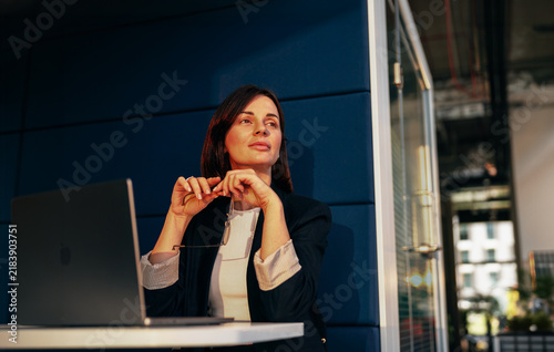 Pensive businesswoman holding her glasses at a laptop desk