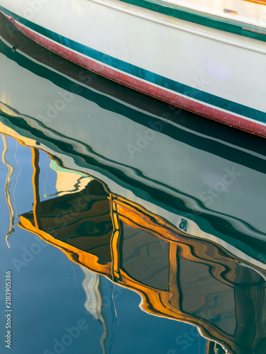 Colorful hull stripe of green, red, and cream reflects with a wavy, painterly image of a wooden cabin structure below