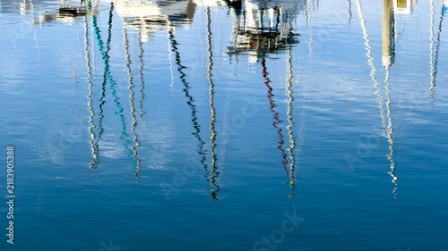 Abstract blue water reflection of mast poles and rigging, rendered as wavy vertical streaks against calm harbor water