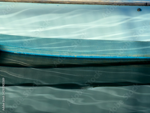 Soft-focus reflection abstract in muted teal and blue tones, showing a boat's hull line blurred with rippling light streaks