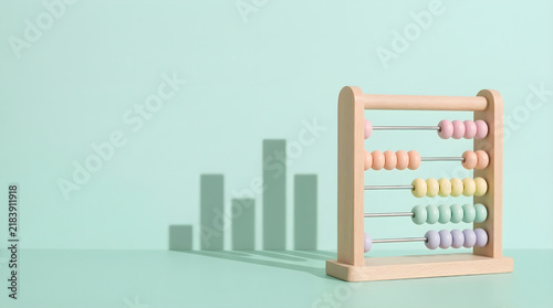 Wooden abacus toy on mint green background casting bar graph shadow symbolizing financial literacy and mathematical education concept