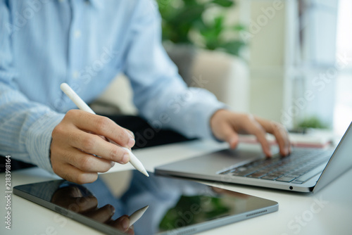 Business professional using stylus on tablet beside laptop for digital workflow business planning data analysis paperless productivity and efficient office management.