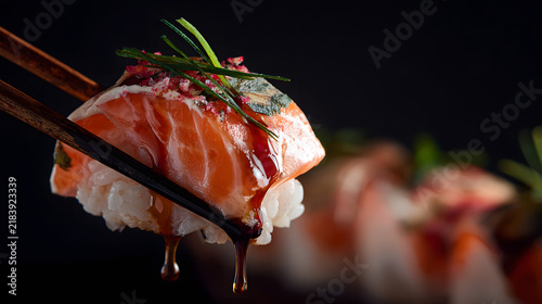 Salmon nigiri with chopsticks drizzling soy glaze garnished with chive and seasoning, appetizing close up showing texture and glossy sauce over rice
