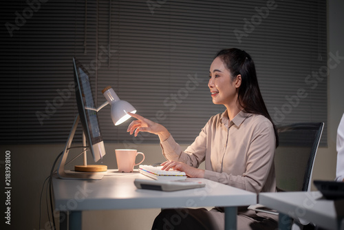 фотографія Asian Businesswoman Working Late at Night on Computer with Desk Lamp in Dark Off