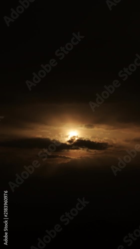 Time-lapse of the sun or moon glowing through dark moving storm clouds