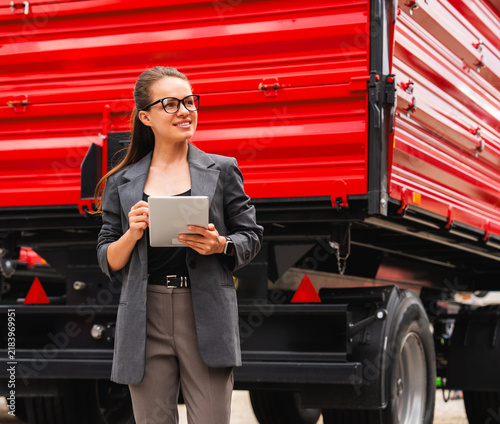 Businesswoman using digital tablet standing near new red trailer at equipment dealership showroom