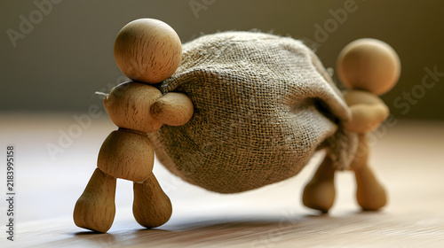 Two wooden statues bear a heavy sack tied with burlap, indicating shared burdens.