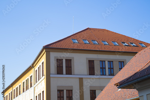 Bild auf Leinwand Red tiled roof with aligned skylights above a sunlit building facade
