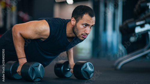Fotografie Focused Black Male Athlete Engaging In Push-up Exercise With Dumbbells In Modern Gym Setting