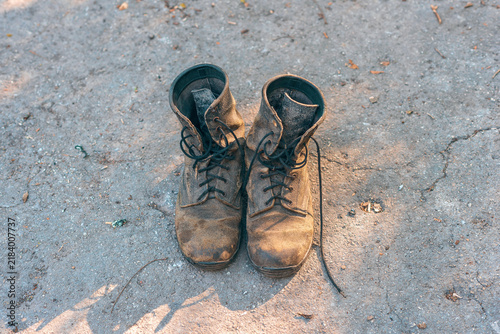 Top view of old worn leather boots standing on ground . Old laces untied and worn texture.