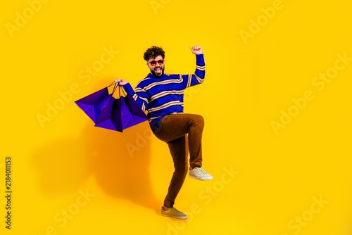 Fotografía Happy young man celebrating with purple shopping bags on bright yellow backgroun