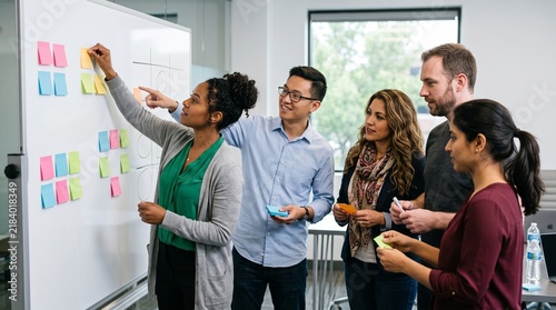 Diverse team collaborating on ideas using sticky notes on a whiteboard in an office setting