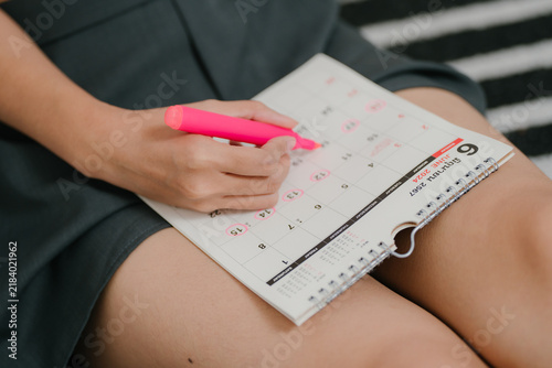 Menstrual cycle tracking concept, woman marks period dates on calendar to monitor menstruation, reproductive health, fertility, ovulation, period, cycle tracking