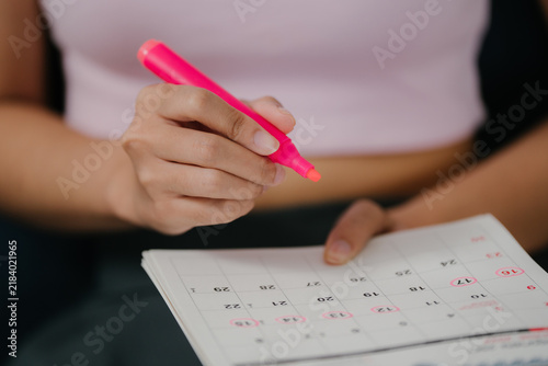 Menstrual cycle tracking concept, woman marks period dates on calendar to monitor menstruation, reproductive health, fertility, ovulation, period, cycle tracking