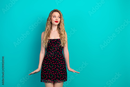 Obraz na plátně Young chic woman in cherry print dress poses against teal background with bright