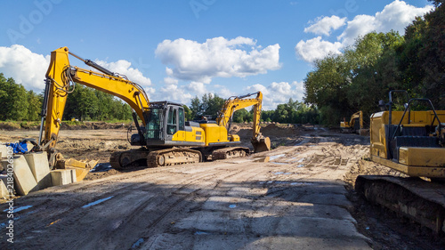 Fotografie Yellow Heavy Excavators Earthmoving on Construction Site for Ground Leveling Wor