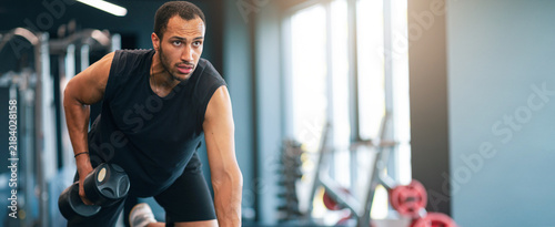 Fotografie Focused Athletic Black Man In His 30s Lifting Dumbbell While Exercising In Modern Gym, Displaying Strength And Determination In His Workout Routine, Emphasizing Fitness Concept