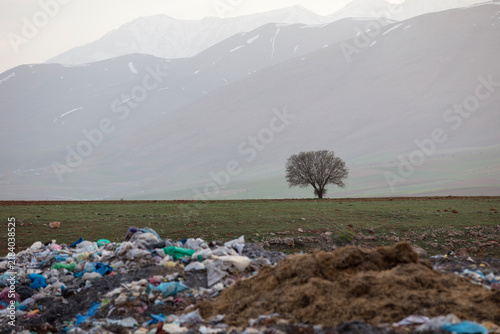 Obraz na płótnie Large pile of plastic and household waste dumped in a rural agricultural area, with snow-covered mountains in the background, highlighting environmental pollution and improper waste disposal