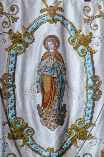 An ornate antique fabric banner displays a detailed embroidered depiction of the Blessed Virgin Mary.