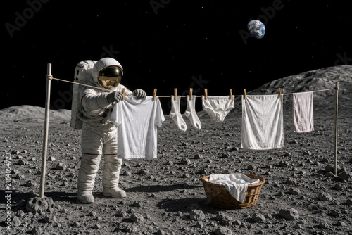 Astronaut hangs white laundry on the Moon beneath Earth. Space for text.