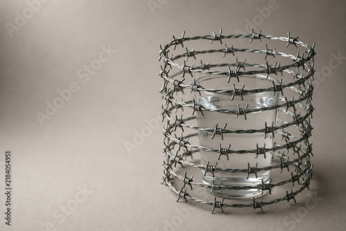 Glass of water enclosed by coils of barbed wire. Space for text.