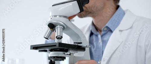 Obraz na plátně Scientist looking through a microscope in a bright laboratory, performing medica