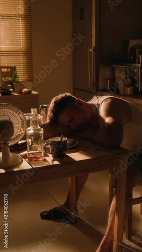 Vertical video of young adult Caucasian man sleeping passed out at table beside alcohol bottle. Clip suitable for substance abuse recovery campaigns and mental health awareness