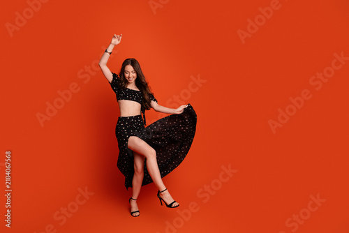 Fotografie Joyful young woman dancing in a black crop top and flowing skirt on an orange ba