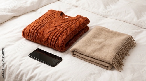 Folded Knitted Sweater, Beige Scarf, and Smartphone on Bed Sheets
