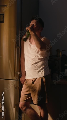 Vertical shot of middle aged Caucasian man drinking beer bottle with troubled expression. Footage ideal for mental health awareness and substance abuse rehabilitation campaigns