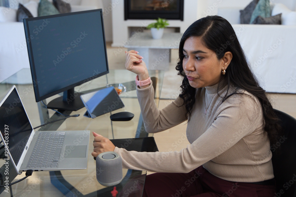 Obraz premium Woman sitting at glass desk in living-room workspace wearing beige top, typing on laptop