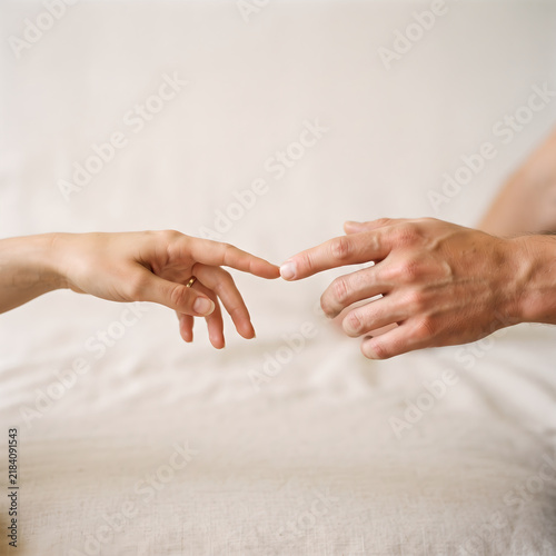 Two hands reaching across a soft white textured surface with gentle natural light