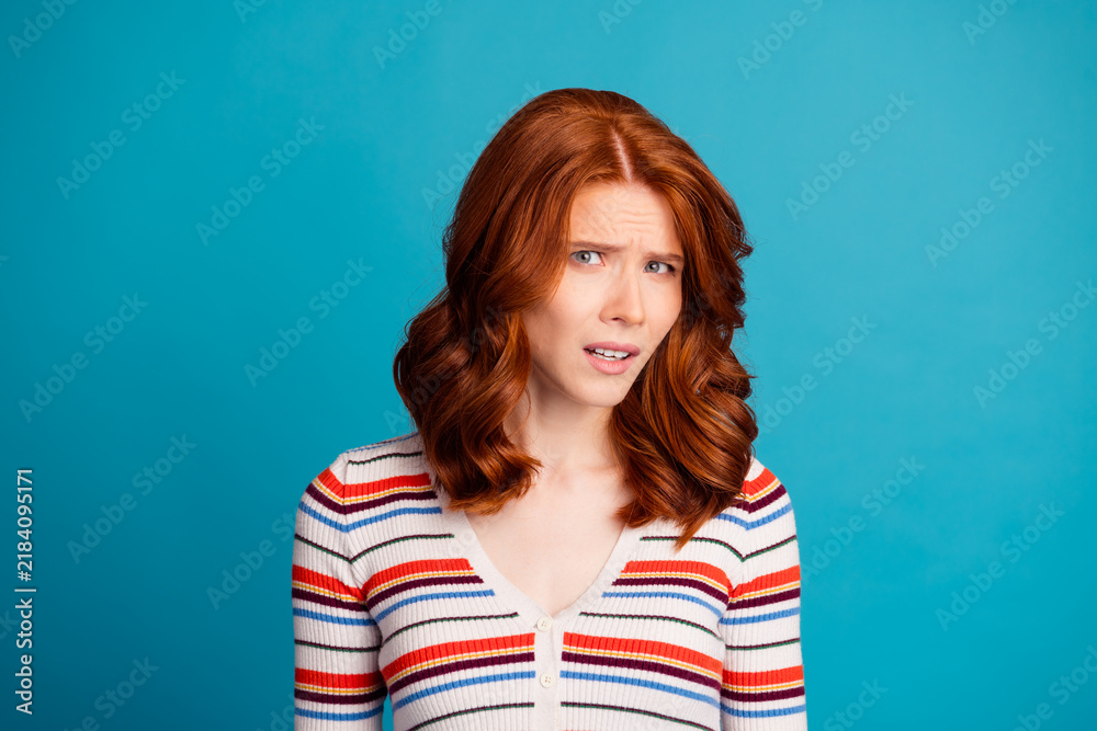 Fototapeta premium Confused redhead woman looking skeptical and doubtful in a casual striped sweater studio portrait against a bright blue background expressing puzzlement