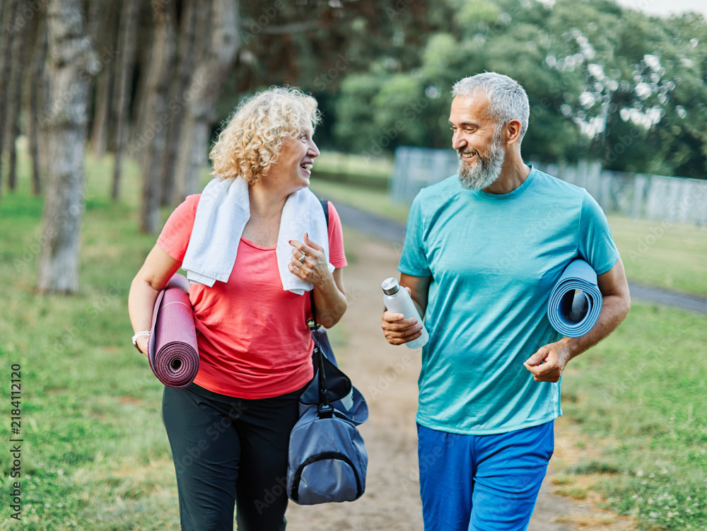 Obraz premium Happy active middle aged couple having fun talking and bonding after having a yoga pilates exercise in park outdoors