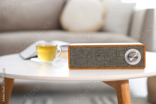 Modern audio speaker and cup on white table in room, closeup