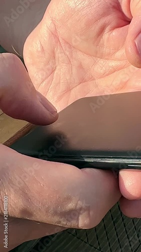 Vertical view of man using mobile smartphone for texting on street. Adult hands holding dark phone device typing quick chat message outdoor. Vertical orientation shot showing online