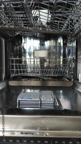 Hands removing clean cups from open upper dishwasher rack in kitchen. Person unloads washed mugs from top basket after wash cycle. Bright kitchen appliance shown in vertical video household