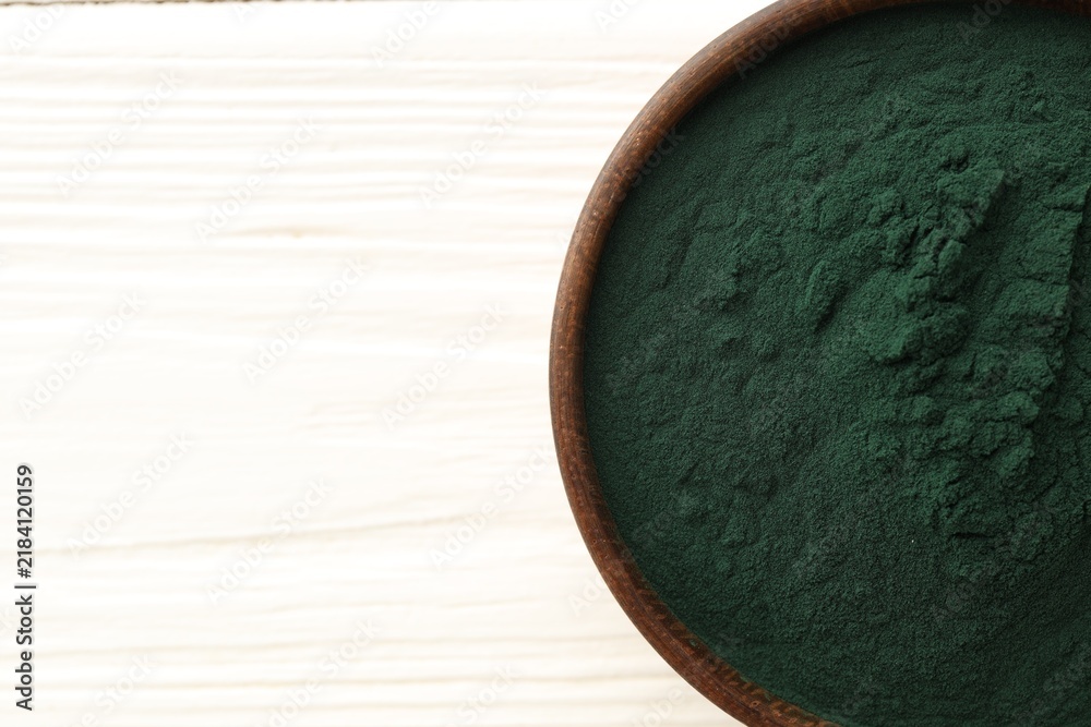 Obraz premium Spirulina powder in bowl on white wooden table, top view. Space for text