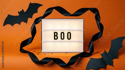 Light box with the word boo surrounded by black paper bats and a black ribbon on an orange background