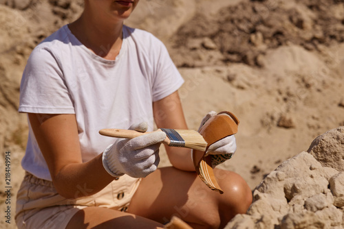Fotografie An archaeologist is carefully brushing dirt off a newly found artifact at an excavation site