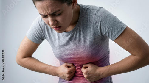 Young woman bent over in agony pressing hands against stomach with glowing red area for depicting severe menstrual or food pain.