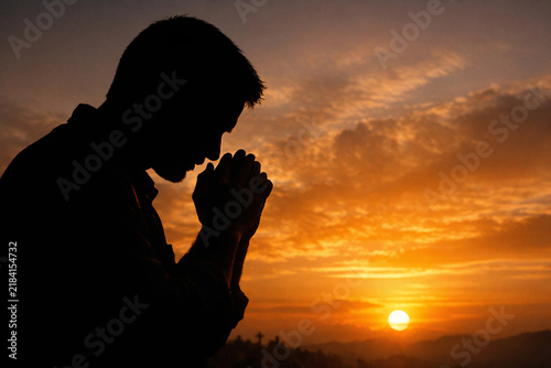 A silhouette of a man in prayer at a beautiful sunset, captured in the warm glow of the setting sun.
