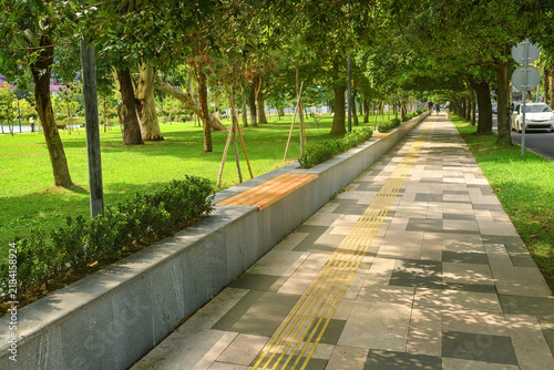 Quadro su tela Paved walkway with built-in wooden benches on stone parapet and tactile yellow p