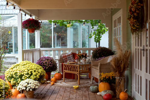 Cozy autumn porch with chrysanthemums, pumpkins and outdoor seating