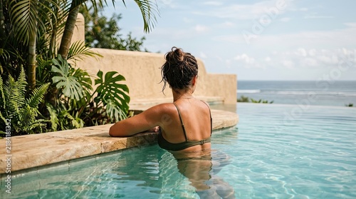 Woman relaxing by infinity pool overlooking tropical ocean view during vacation
